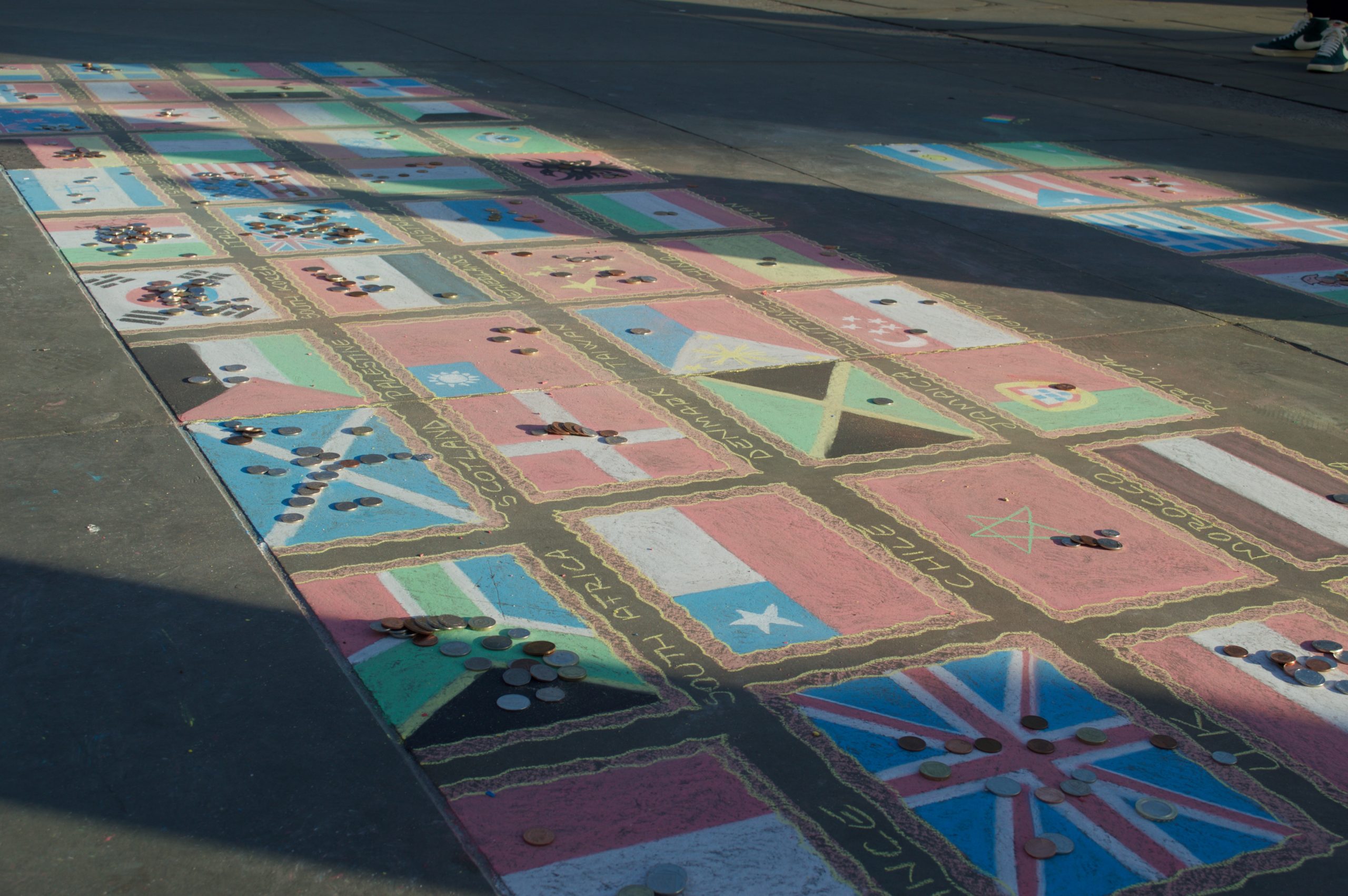 Countries drawn in chalk on a sidewalk with differing amounts of coins placed on top of each country.