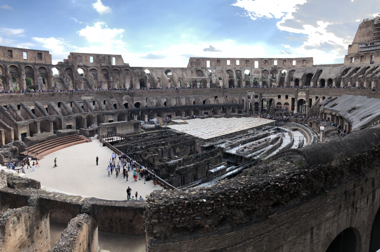 Inside of the Colosseum in Rome. There are tourists walking around the ancient site.