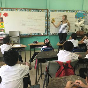 Teacher standing at the front of a classroom, teaching a group of students abroad.