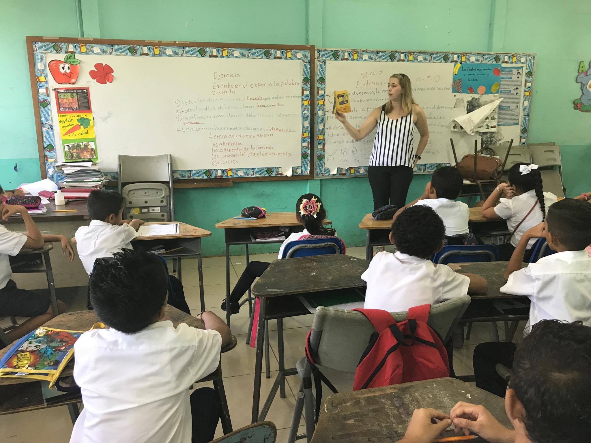 Teacher standing at the front of a classroom, teaching a group of students abroad.