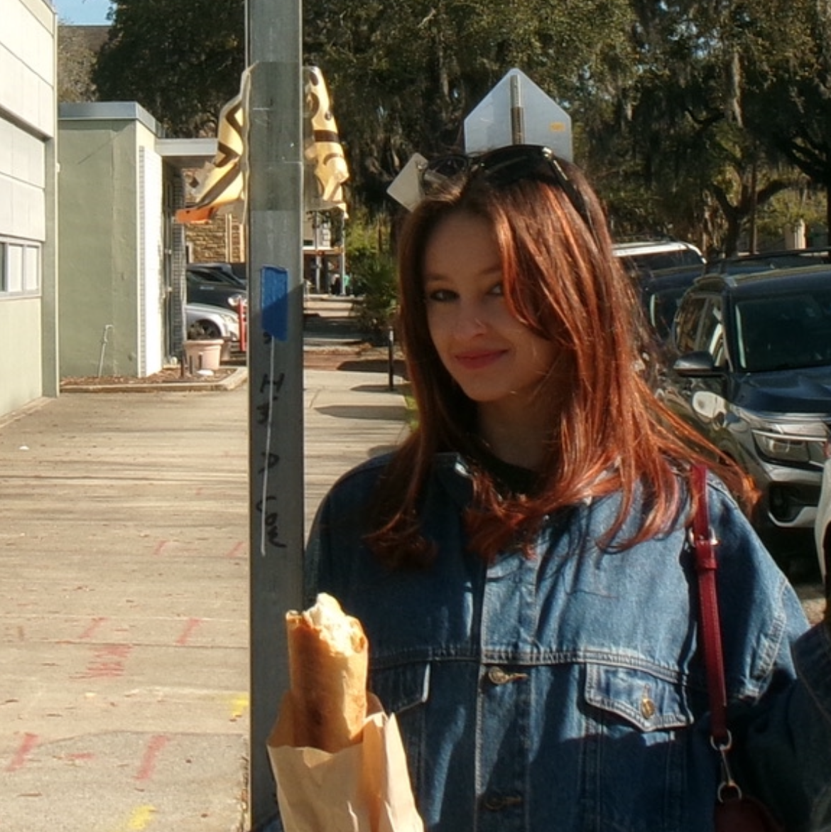 Young woman with medium legnth red hair wearing a denim jacket and holding a baguette.