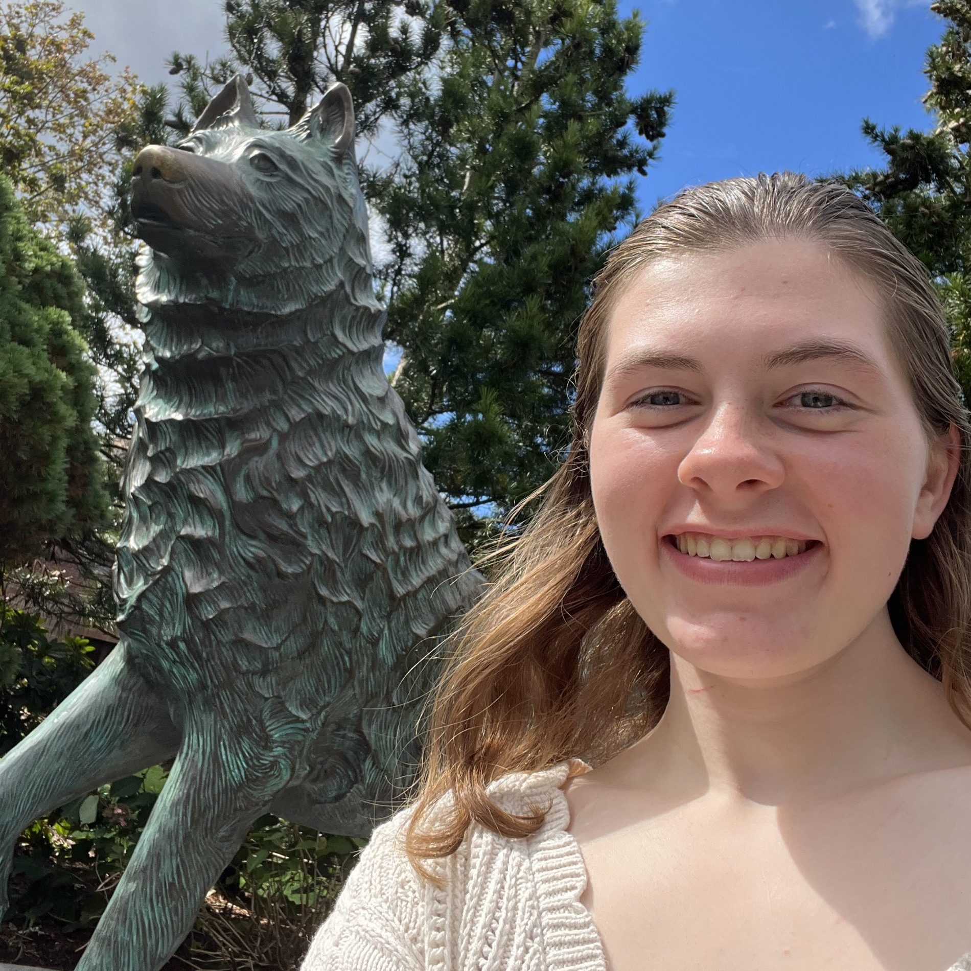 Female student smiles wearing a white sweater next to UConn husky statue.