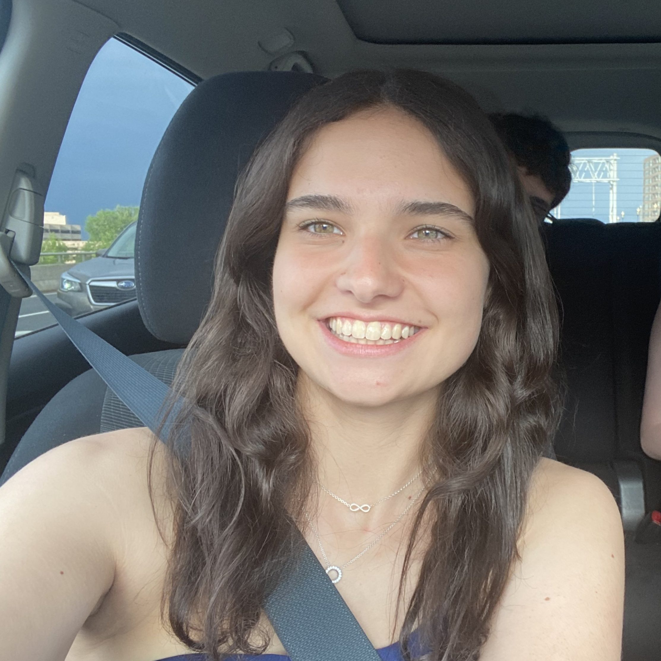 Female student with medium length brown hair smiles in a car with her seatbelt on.